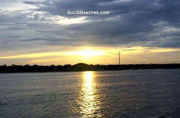 St Augustine Florida Sunset from Sailboat with tall metal mssion cross & yellow beam on ocean + blue color clouds